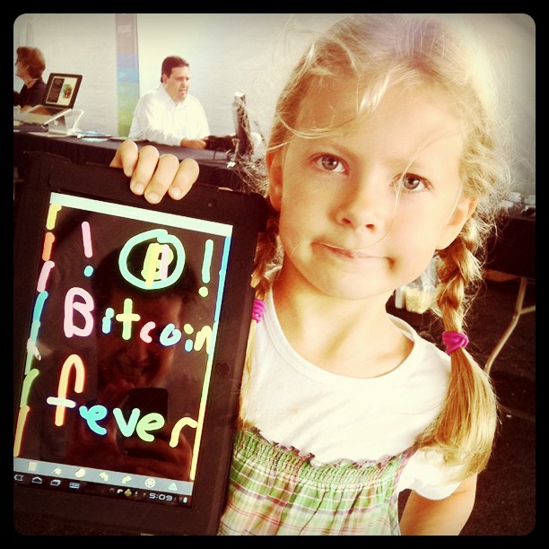 niña con un tablet en el que ha dibujado Bitcoin Fever, su padre se refleja apasionado en el tablet